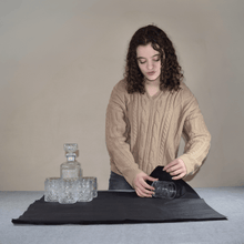 Load image into Gallery viewer, A Woman Using Black Tissue Paper Sheets to Wrap a Glass Cup to Prevent Shipping Damage. The Woman is Using Giftique Wholesale&#39;s 20x30 Black Tissue Paper.
